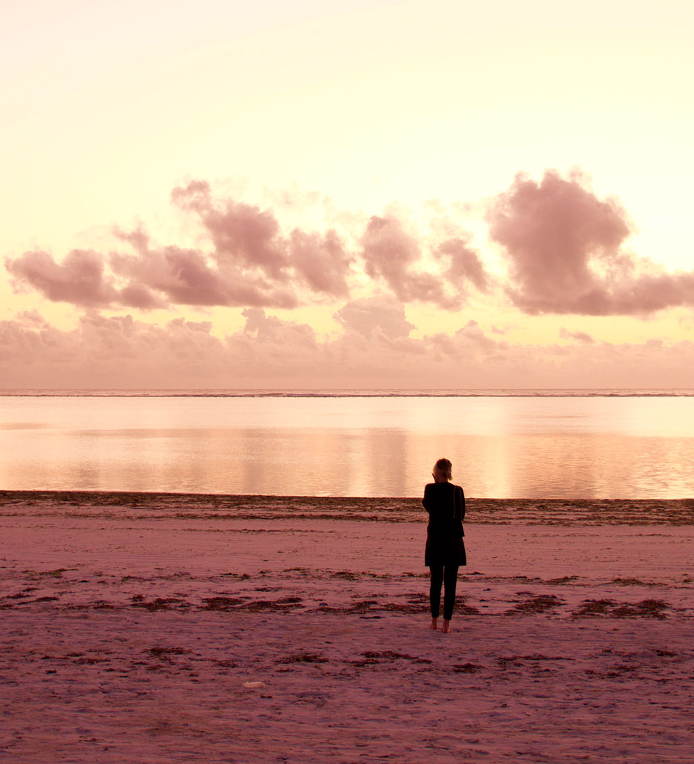 Eine Person steht am Meer und blickt auf den warm beleuchteten Horizont.
